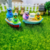 A set of three mini resin cruise ducks with sunglasses in blue, green, and yellow on a wooden boat.