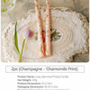 Two long-stemmed printed candles in peach and white with floral designs displayed on a lace platter.