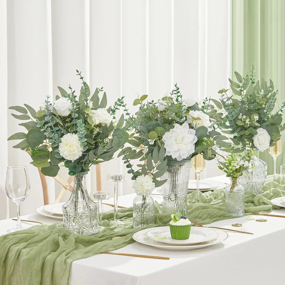 A floral centerpiece featuring white flowers and green eucalyptus leaves in glass vases on a white table.
