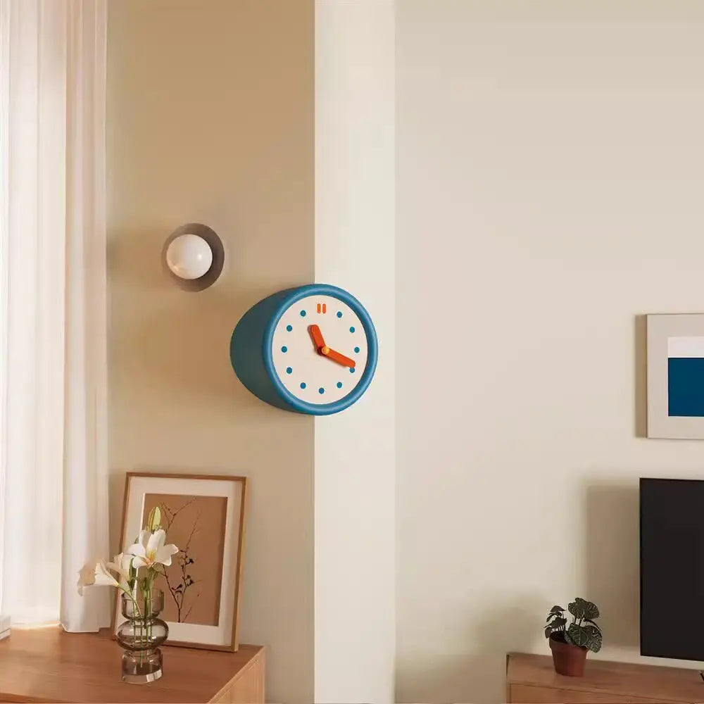 A modern resin wall clock with a blue face and orange hands is mounted on a beige wall.