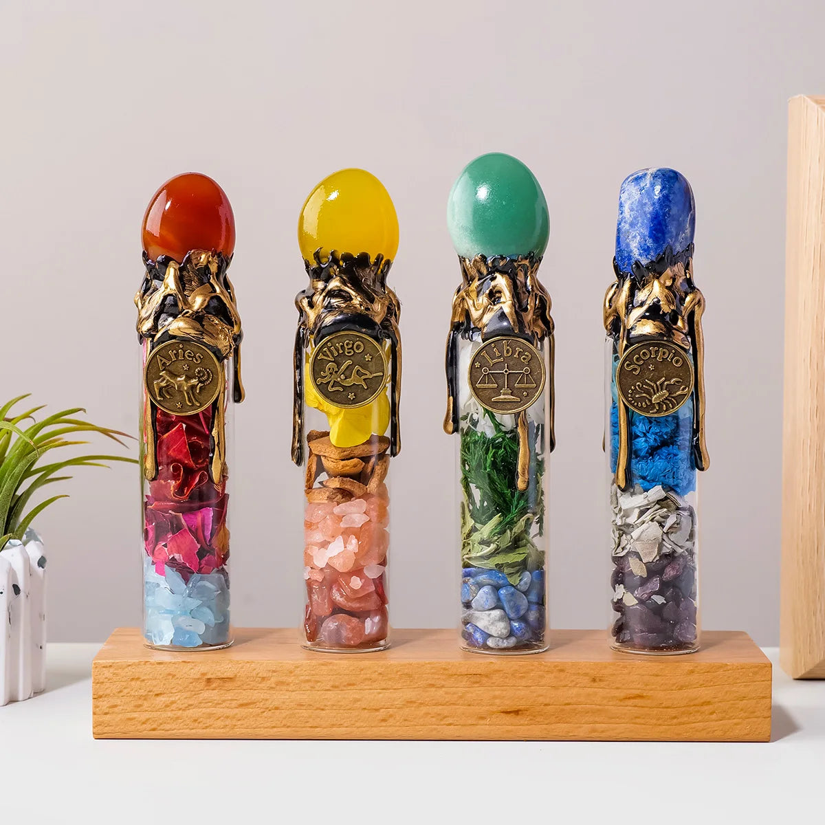 Four glass bottles filled with colored crystals representing zodiac signs standing on a wooden base