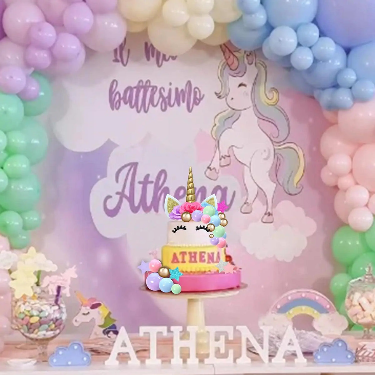 A pink and yellow unicorn cake decoration set featuring flowers, stars, and balls displayed on a white stand.
