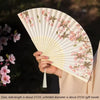 A hand holds an elegant floral bird print bamboo folding fan with a light beige color.