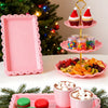 A three-tier pink dessert rack holds various colorful candies and desserts on a white surface.