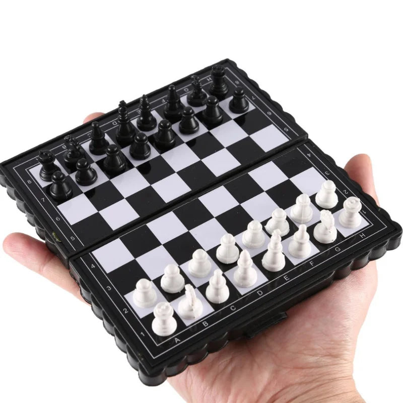 A hand holds a portable folding magnetic chess set with black and white pieces on a black and white board.