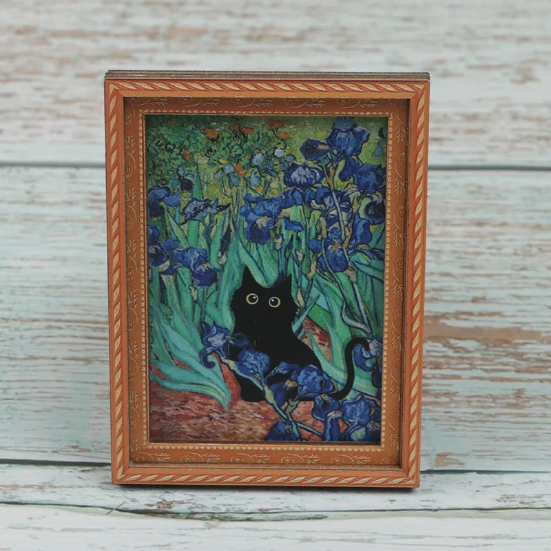 A framed painting featuring a black cat amidst blue and green flowers on a light wooden background.