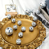 A set of ten silver disco ball ornaments displayed on a gold platter with ornate detailing.