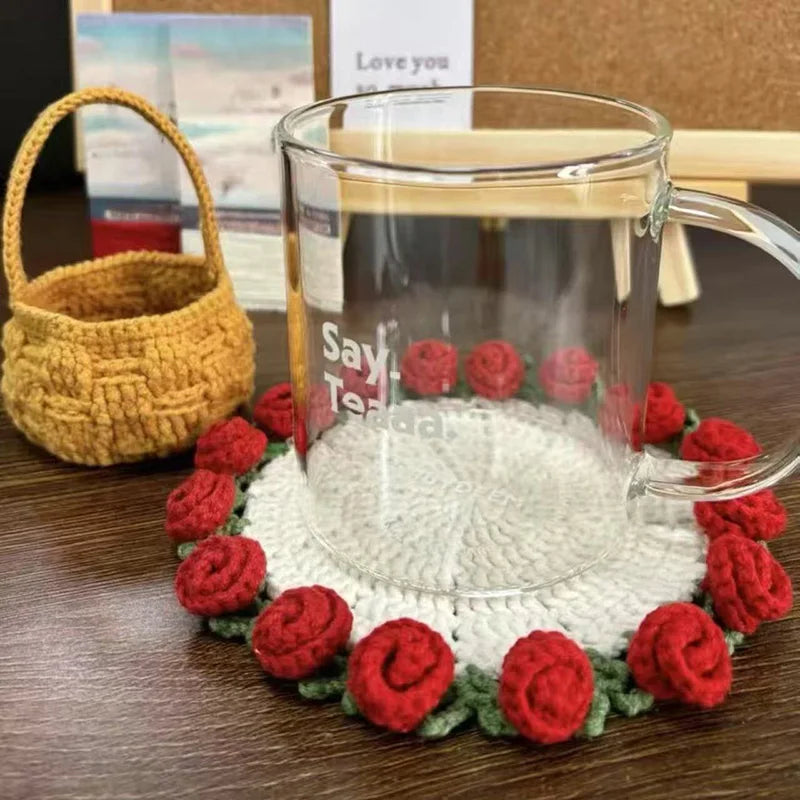 Hand-crocheted red rose flower coasters arranged around a glass mug on a wooden surface.