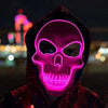 A person wearing a glowing pink LED skull mask with a hood against a dark, blurred city background.