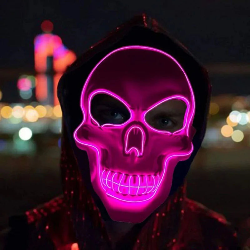A person wearing a glowing pink LED skull mask with a hood against a dark, blurred city background.