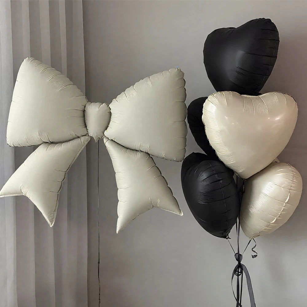 A cluster of heart-shaped foil balloons in black and white are displayed against a light gray wall.
