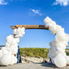 A wooden arch decorated with white and purple latex balloons against a blue sky backdrop.