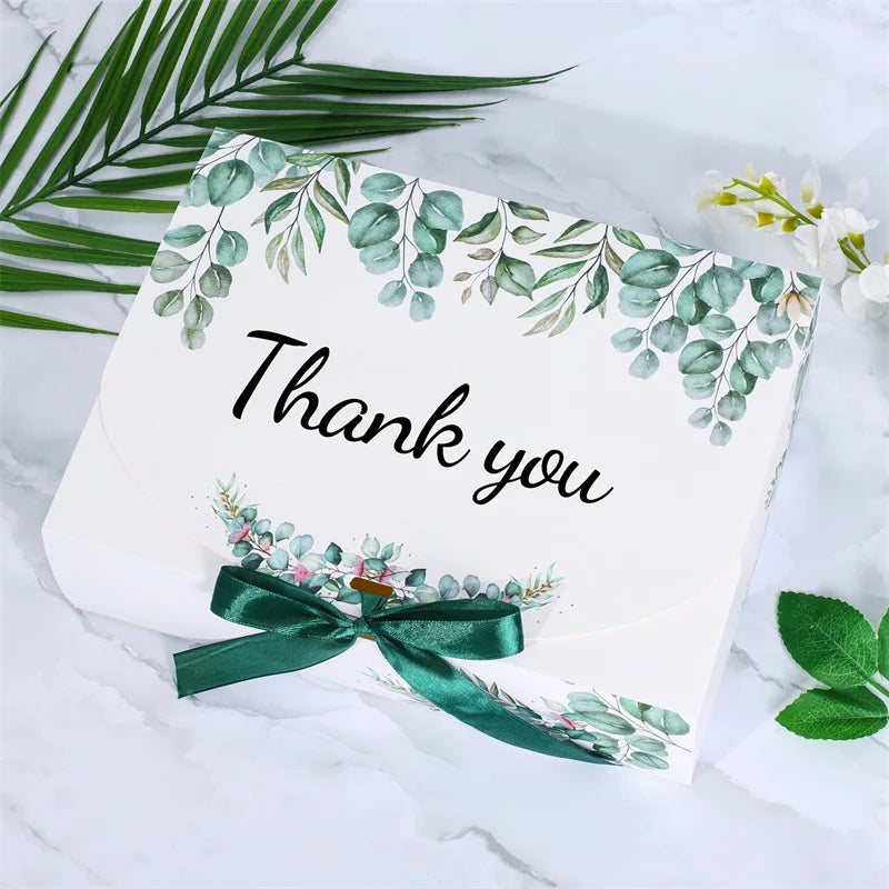 White gift box decorated with green eucalyptus leaves and a dark green ribbon tie.