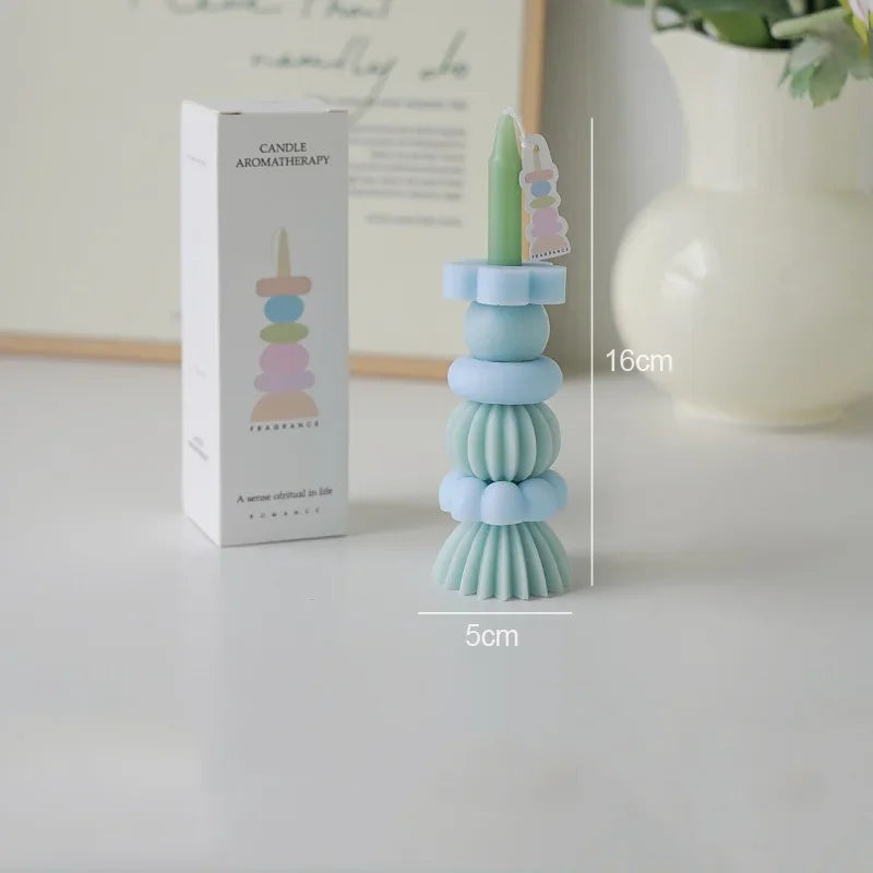 A tall, stacked candle holder with pastel blue and green candles and a pink wand, displayed next to its packaging.