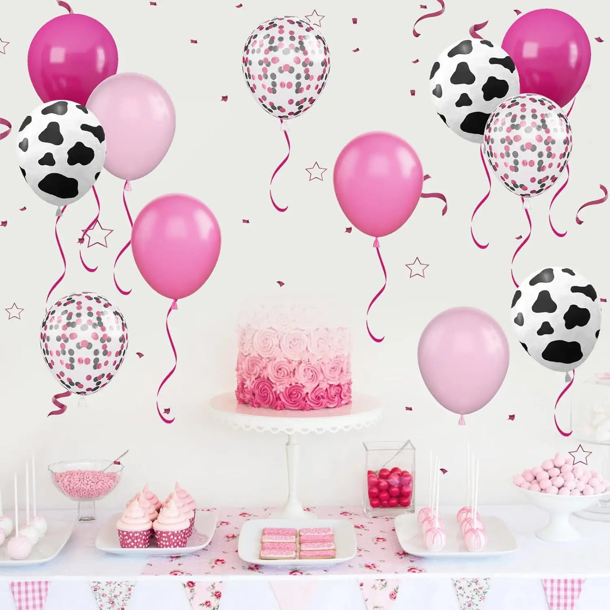 A collection of pink and black cow print balloons, including solid pink and patterned balloons, displayed on a table.