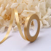 A roll of gold satin balloon ribbon unwinding against a background of white flowers.
