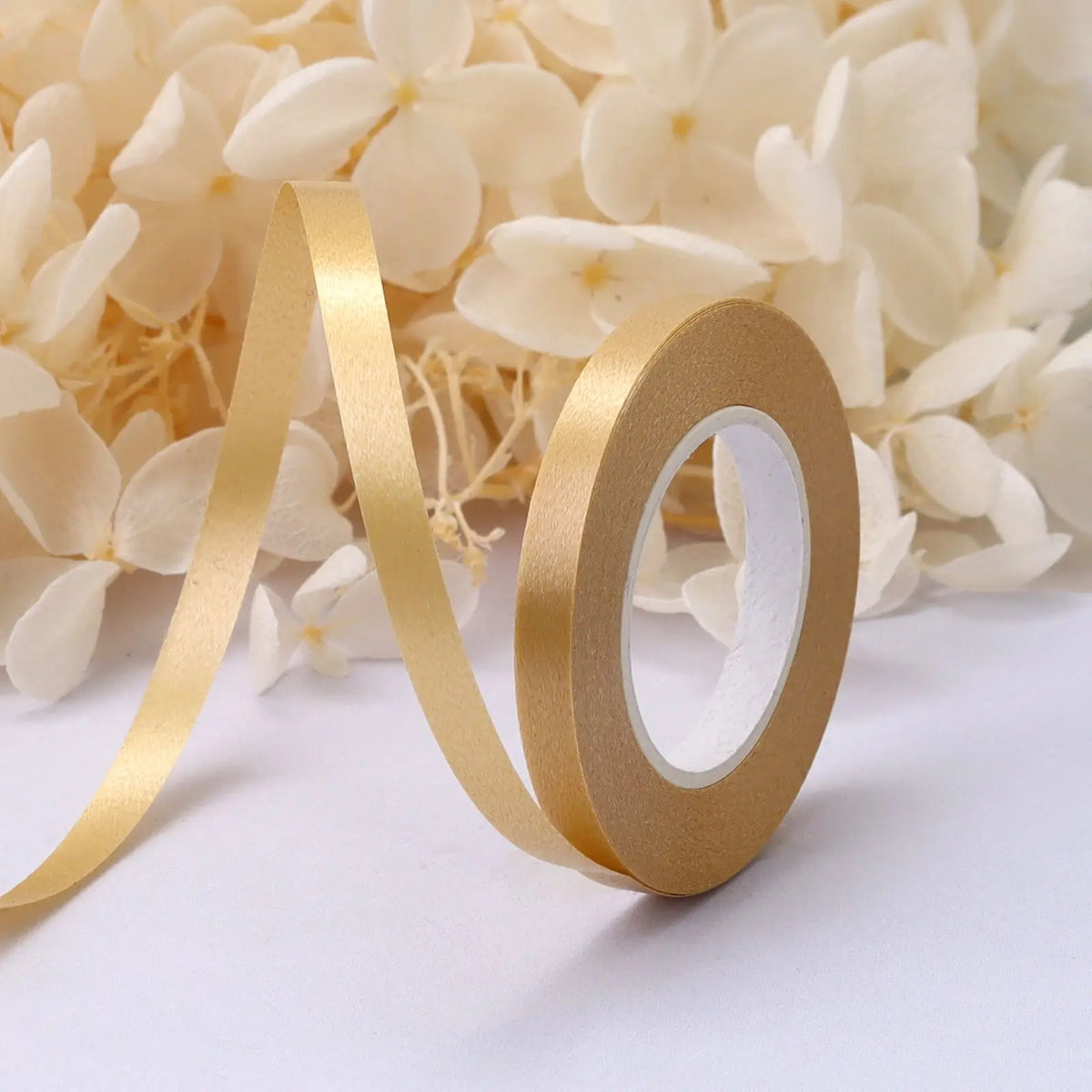 A roll of gold satin balloon ribbon unwinding against a background of white flowers.