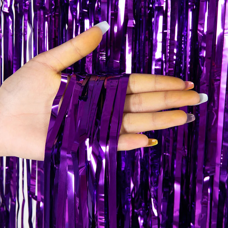 A hand is holding purple metallic tinsel foil fringe curtain backdrop fabric.