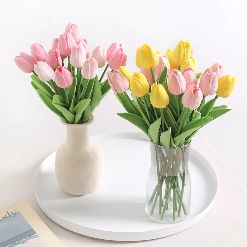 A bouquet of artificial pink and yellow tulips in a vase on a white tray.