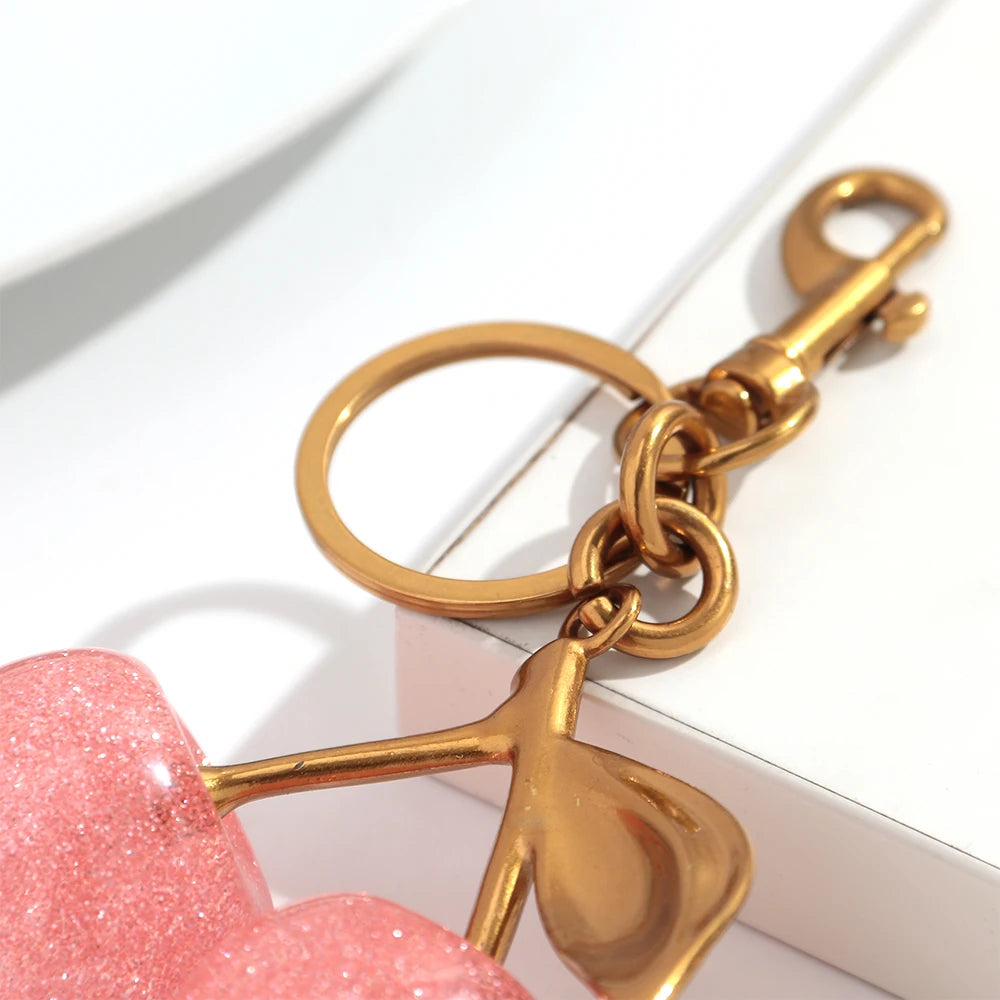 A gold-toned chain keychain featuring a leaf charm attached to a pink cherry resin pendant.