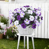 A bouquet of purple and white artificial petunia flowers with vines displayed in a white pot on a small white stand.