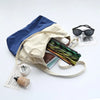 A light beige fabric tote bag with blue accents holds a folding bamboo hand fan and sunglasses on a white background.