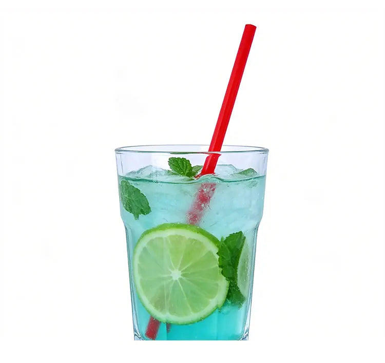 A glass of iced green beverage garnished with lime slices and mint, served with a red disposable straw.