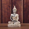 A silver-colored Buddha statue handcrafted from resin, seated in meditation pose on a wooden surface.