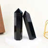A black natural obsidian crystal obelisk point standing on a white surface.