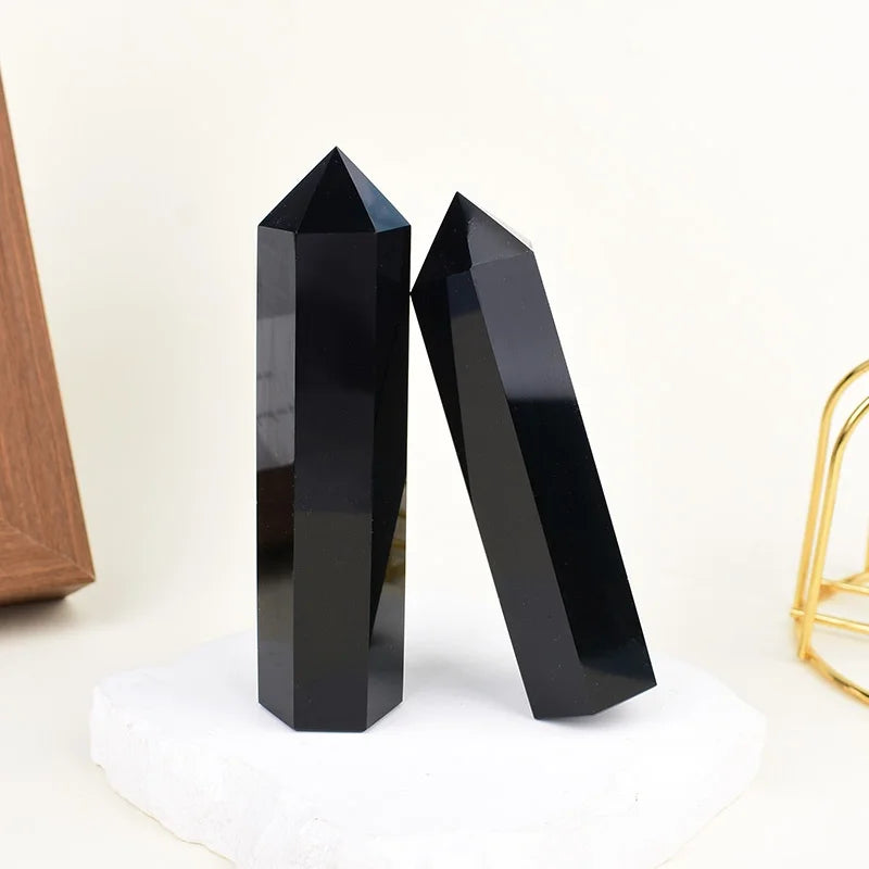 A black natural obsidian crystal obelisk point standing on a white surface.