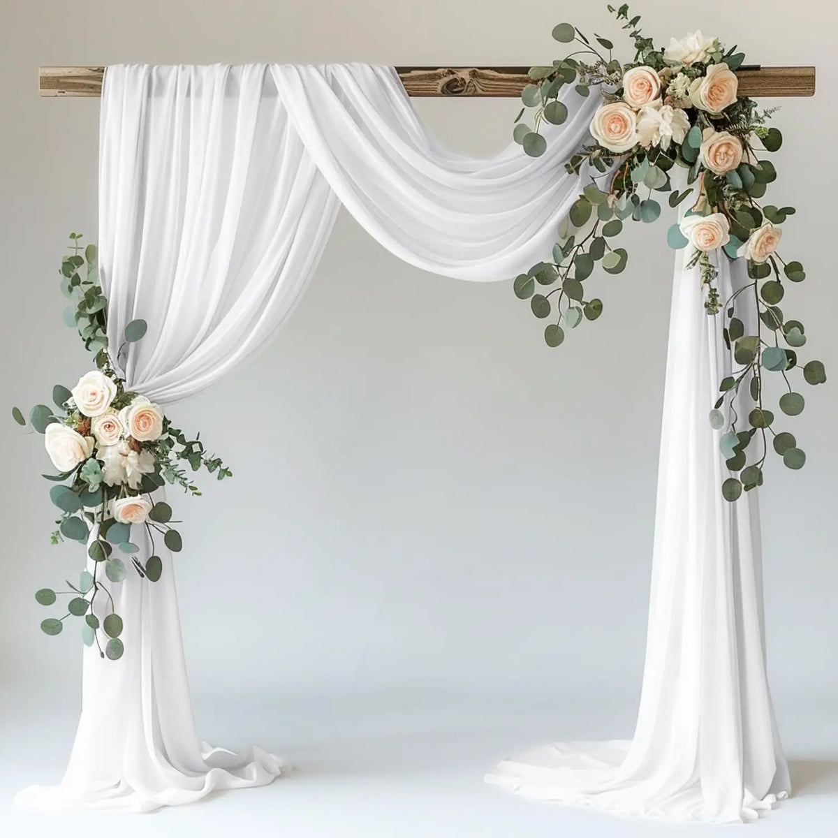 White sheer tulle draping fabric used to create a wedding arch backdrop with floral greenery