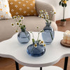 A set of three minimalist blue glass bud vases displayed on a white table.