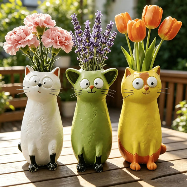 Three ceramic cat figurines in white, green, and yellow colors displayed on a wooden deck.