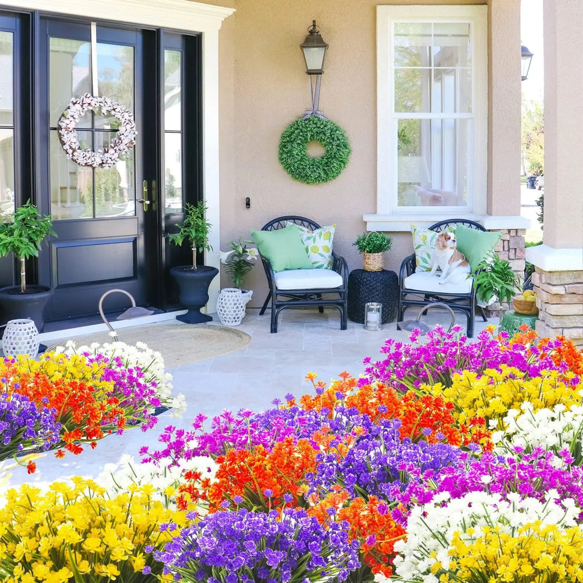 A vibrant flower bed featuring purple, orange, yellow, and white blooms in front of a light-colored house entrance.