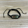 A black beaded bracelet with a green and gold oval pendant on a wooden surface.