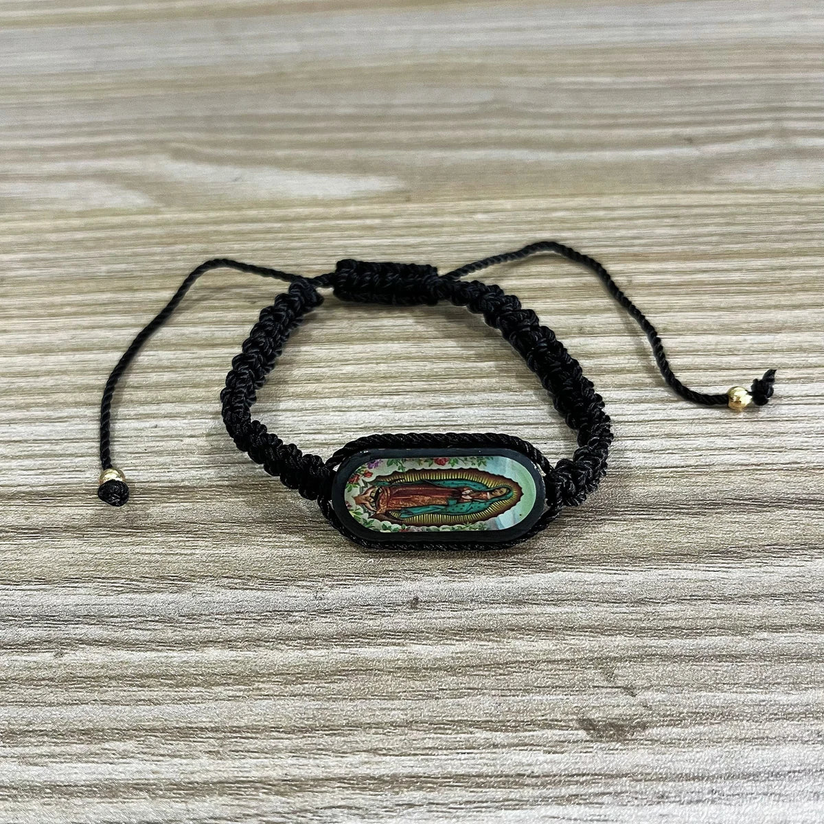 A black beaded bracelet with a green and gold oval pendant on a wooden surface.