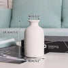 A white ceramic vase is shown on a table with various measuring tools and a black box in the background.