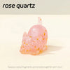 A pink rose quartz crystal fragment shaped like a crouching cat, embedded in resin.