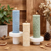 Three pillar candles in blue, cream, and green are displayed on a wooden surface.