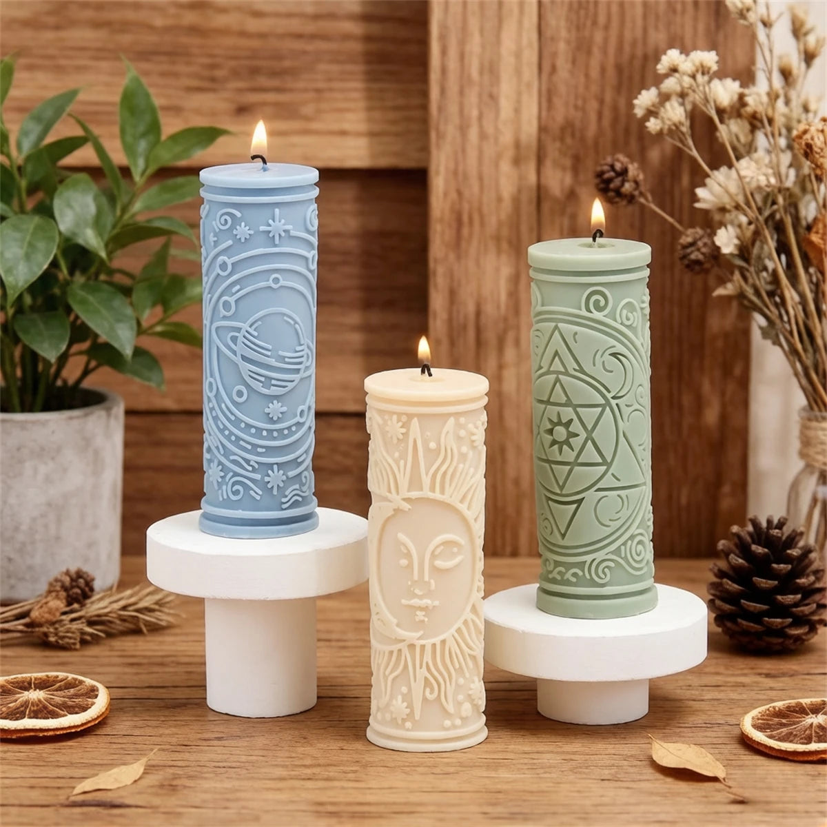 Three pillar candles in blue, cream, and green are displayed on a wooden surface.