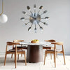 A modern cutlery 3D wall clock featuring silver forks arranged in a circular design above a wooden dining table.
