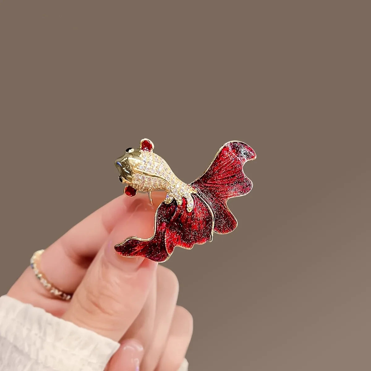 A vintage marine life brooch pin featuring a gold-colored fish with red and silver glitter details.