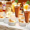 A display of elegant disposable champagne glasses filled with colorful cocktails and garnished drinks on a white table.