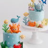 A tiered cake decorated with ocean animal toppers including a whale, octopus, and turtle.
