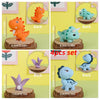 Un juego de cuatro toppers de dinosaurios de plástico en naranja, verde, morado y azul.