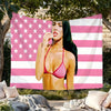 A woman wearing a pink top poses against a white and pink striped flag tapestry.