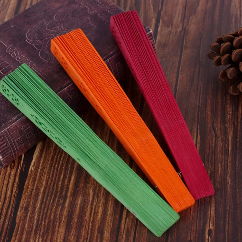 Three hand carved bamboo folding fans in green, orange, and red resting on a wooden surface.