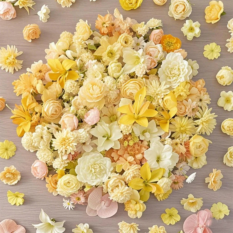 A dense arrangement of mini silk artificial flower heads in shades of yellow, cream, and peach on a wooden surface.