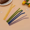 A collection of various colored reusable borosilicate glass straws with cleaning brushes arranged on a light background.