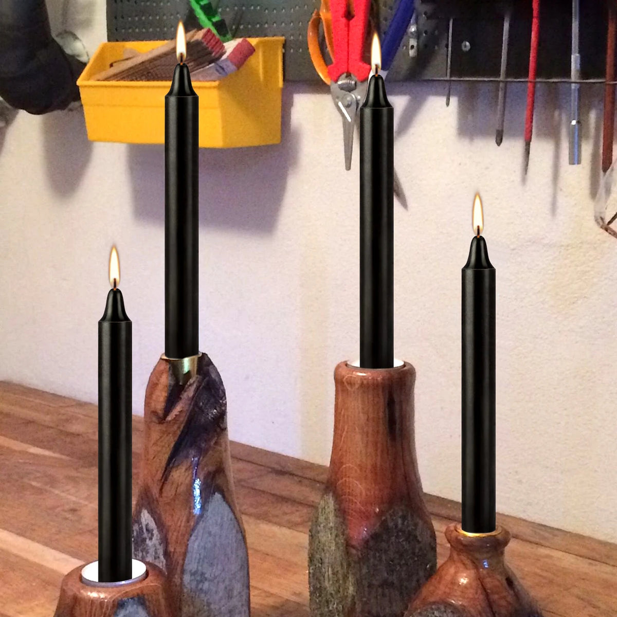 A set of black taper candles in wooden holders displayed against a light wall.